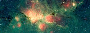 Cats Paw nebula, de groene gebieden zijn het gevolg van straling van hete sterren die fluorescentie van PAKs induceert. (Source: NASA/JPL-Caltech, Wikipedia)